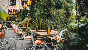 Schani Garten mit Tischen und vielen Pflanzen im Hintergrund. Keine Menschen abgebildet.